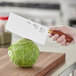 A hand holding a Mercer Culinary Chinese cleaver over a cabbage on a wooden surface.