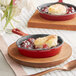 A small red Valor enameled cast iron skillet with a dessert in it on a wooden plate with a spoon.