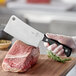 A person using a Mercer Culinary cleaver to cut a piece of meat.