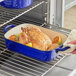 A hand holding a blue Valor enameled cast iron roasting pan with a roasted chicken in it.