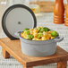 A Valor slate grey enameled cast iron pot filled with macaroni and cheese with broccoli on a wooden surface.