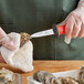 A person using a Choice Boston Style Oyster Knife with a red handle to cut up oysters.