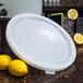 A white Carlisle round food storage container lid on a table next to lemons.