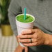 A person holding a Phade giant blue drink with a green liquid using a compostable straw.