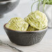 A close-up of a black Acopa stoneware bowl filled with green ice cream with a spoon.