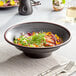 A black matte textured stoneware bowl of food with a silver fork and knife on a table.