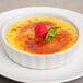 A Tuxton porcelain white fluted souffle dish filled with creme brulee with a raspberry on top.