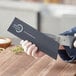 A hand holding a black Mercer Culinary knife guard over a knife on a cutting board.