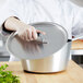 A chef using a Vollrath Wear-Ever aluminum pot lid over a pot.