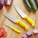 A Choice 3-piece knife set with yellow handles next to cucumbers on a table.