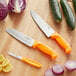 A Choice 3-piece knife set with knives with orange and yellow handles on a cutting board with vegetables.