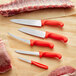 A Choice knife set with red handles on a wooden surface with a piece of meat.