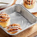 A Choice square foil cake pan with cinnamon rolls on a tray.