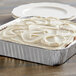 A Choice foil square cake pan with white frosting on a cake.