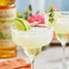 A pair of margaritas garnished with lime slices on a table with Monin Organic Agave Nectar.