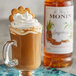 A glass mug of brown liquid with a cookie on top and a bottle of Monin Premium Gingerbread Flavoring Syrup.