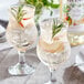 Two glasses of Monin white peach flavored drinks with ice and fruit on a table.