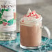 A glass mug of hot chocolate with whipped cream and candy canes flavored with Monin Premium Peppermint Flavoring Syrup.