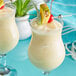 Two glasses of THAI Kitchen unsweetened coconut milk with pineapple on top.