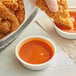A person dipping a fried chicken piece into a bowl of Frank's RedHot Buffalo sauce.