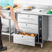 A woman using tongs to put food in a ServIt triple drawer warmer.