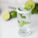 A glass of water with a lime slice and mint leaves with a yellow and green Rokz Mojito garnished rim.