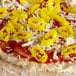 A pizza with pepperoni and banana pepper rings on a table.