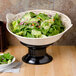 A black melamine pedestal with a bowl of salad on a table.