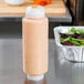 A FIFO Innovations 24 oz. squeeze bottle of salad dressing on a counter next to a salad.