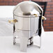 A silver stainless steel Vollrath New York Sauce Chafer with brass trim.