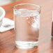 A Libbey straight sided seltzer glass filled with ice water on a table.