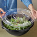 A woman holding a clear plastic container with a Visions plastic lid over a bowl of salad.