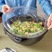 A woman holding a Visions clear plastic bowl of salad with a flat lid.