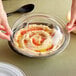 A person holding a bowl of hummus with a clear Visions dome lid.