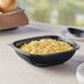A black Visions PET plastic bowl filled with macaroni and cheese with a spoon on the table.