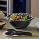 A black Visions plastic bowl filled with salad and vegetables on a table.