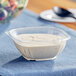 A Visions clear plastic bowl filled with white sauce on a blue cloth.