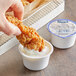 A hand dipping fried chicken into a cup of Hellmann's ranch dressing.