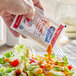 A hand pouring Hellmann's French dressing from a packet onto a salad.