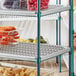 A Regency green wire shelving unit with plastic containers of vegetables and fruit on a shelf.