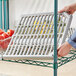 A person holding a plastic container of tomatoes on a Regency green wire shelf.