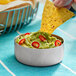 A person holding a chip and dipping it into a stainless steel bowl of guacamole.
