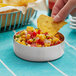 A person dipping a chip into a bowl of corn salsa.