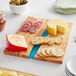 An American Metalcraft rectangular olive wood serving board with cheese, crackers, and olives on it.