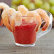 A clear plastic Fineline Tiny Temptations cup filled with shrimp cocktail garnished with a shrimp and tomatoes.