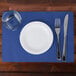 A white plate with a fork and knife on a navy blue scalloped paper placemat.