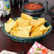 A round weave basket filled with jalapeno-shaped bowls of chips and salsa on a table.