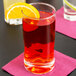 A Libbey customizable beverage glass filled with red liquid and a slice of orange on a napkin.
