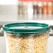 A Carlisle green polypropylene food storage container lid on a plastic container filled with pasta on a kitchen counter.