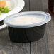 A black Pactiv Newspring Ellipso souffle container with a clear lid.